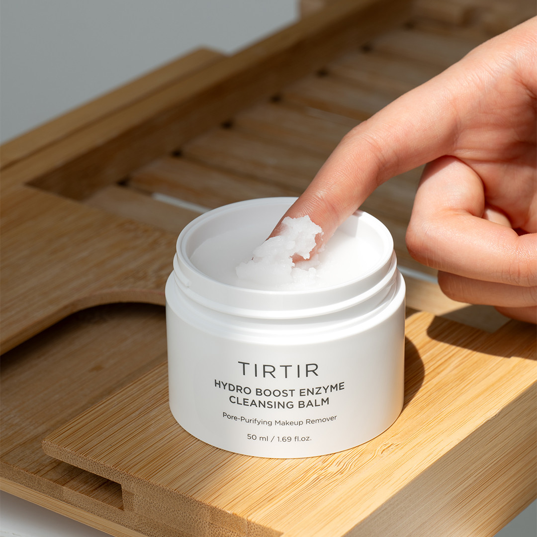 Person applying TIRTIR cleansing balm to their finger on a wooden surface