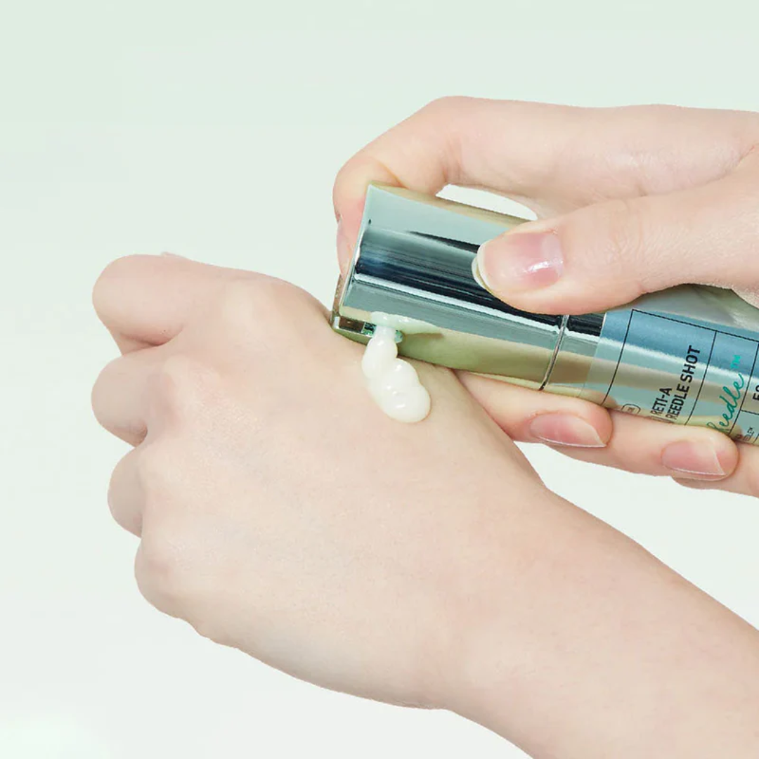 Hand applying cream from a small container on a light background