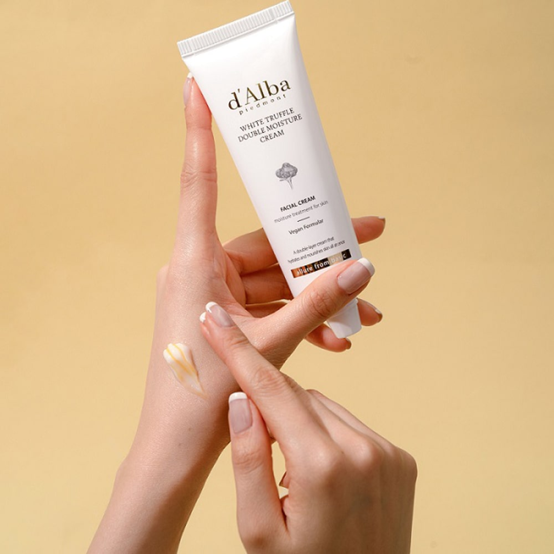 Hand holding a tube of d'Alba cream against a beige background
